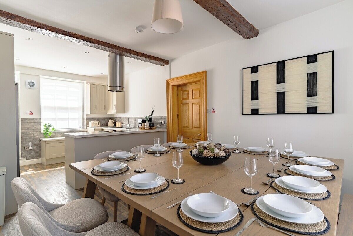 Un coin repas avec une longue table dressée pour le repas, une cuisine en arrière-plan et une porte en bois.