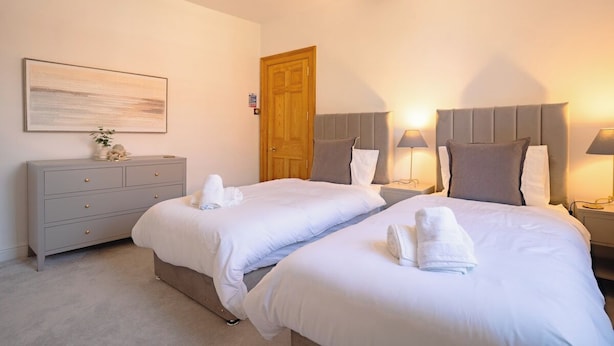 A double room with two beds, a dresser, a wooden door, and wall-mounted lamps. - St James House Timeless Comfort Central Congleton (Congleton)