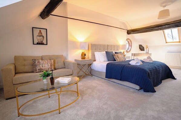 A bedroom with a bed, a sofa, a bedside table, a lamp, and a framed picture on the wall.