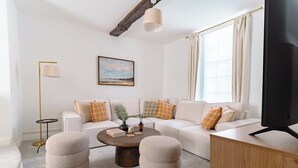 A modern living room with a sofa, ottomans, a coffee table, a floor lamp, and a painting on the wall. - St James House Timeless Comfort Central Congleton (Congleton)
