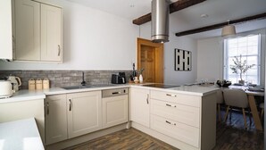 A kitchen with a built-in dishwasher, a coffee machine, and a large island with a sink. - St James House Timeless Comfort Central Congleton (Congleton)