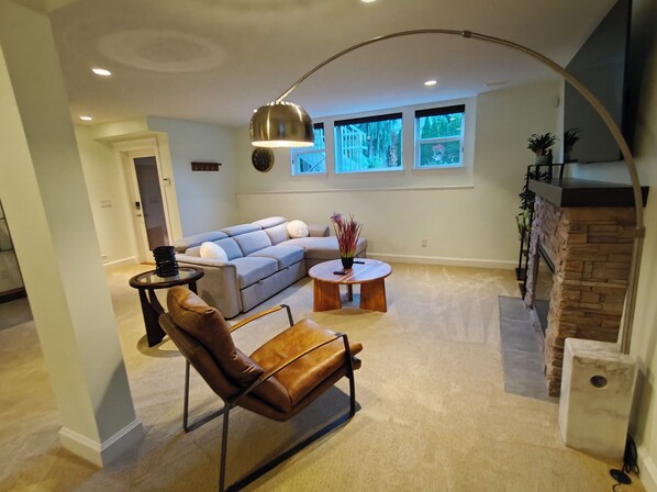 A living room with a sectional sofa, a leather chair, a round coffee table, and a fireplace.