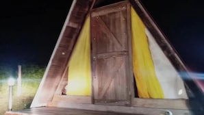 A triangular wooden structure with a door and a bench. - Zona Camping El Amanecer (Provincia de Guanacaste)