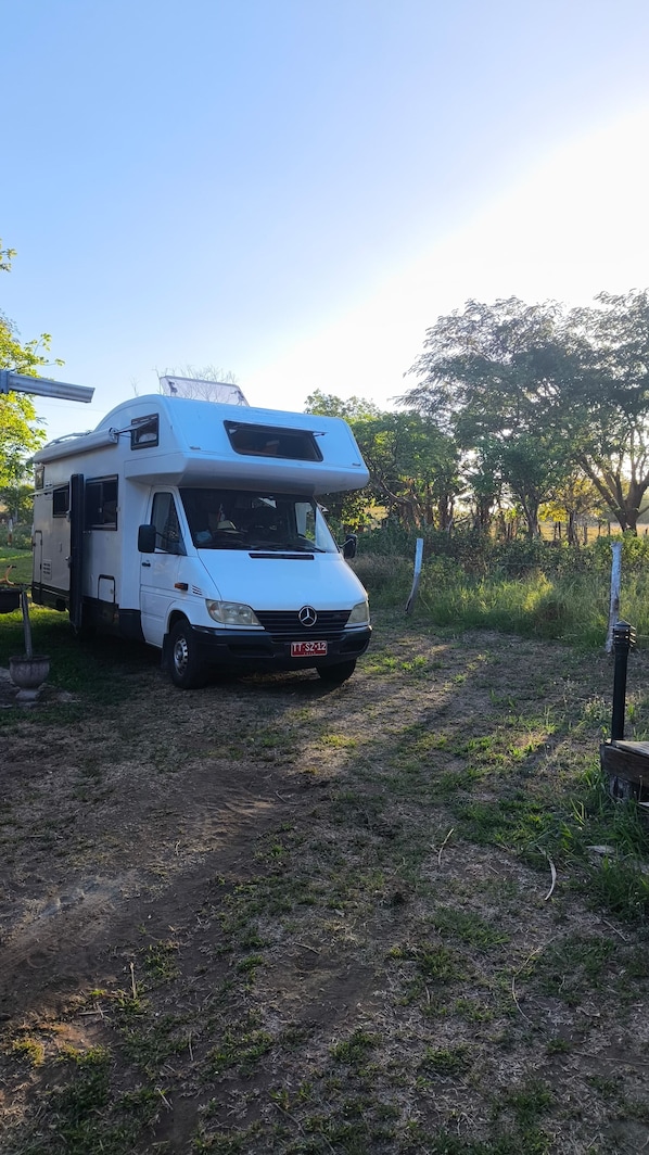 A white camper van parked on a dirt path with grass and trees in the background.