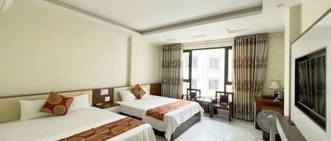 A hotel room with two beds, a desk, a chair, a TV, and a window with curtains.