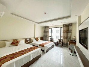 A hotel room with two beds, a desk, a chair, a TV, and a window with curtains. - XUAN HINH HOTEL (Bai Chay)