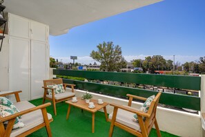 Ein Balkon mit Holzmöbeln, einem grünen Kunstrasen und Blick auf eine Straße sowie Gebäude.