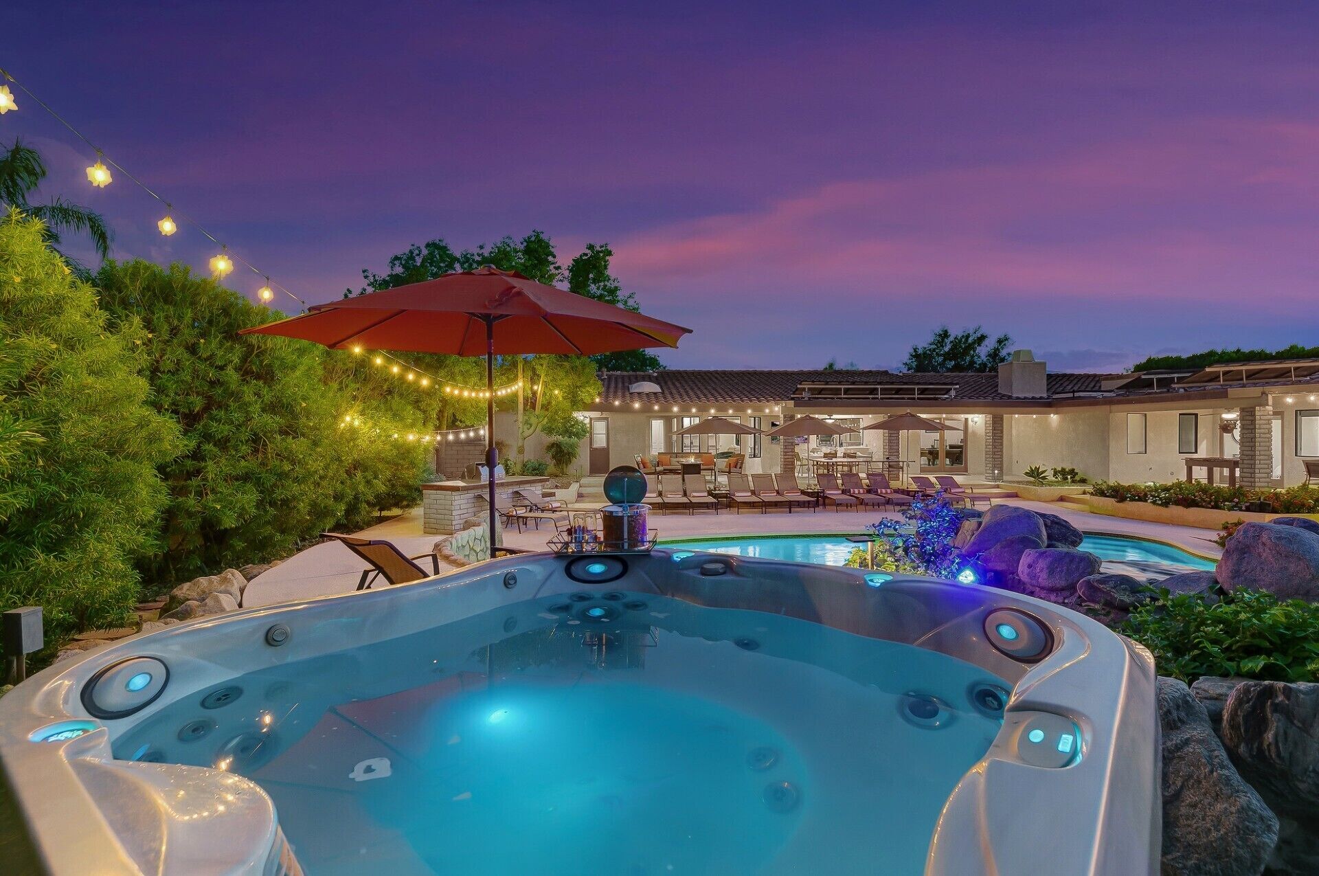 A hot tub with a stone surround, a pool with a waterfall feature, and outdoor seating with umbrellas.