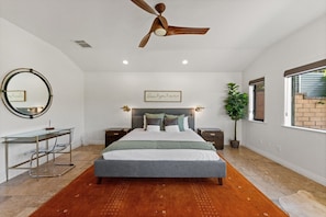 Ein Schlafzimmer mit Bett, Nachttischen, Deckenventilator, Spiegel, Wandleuchte und Fenster.