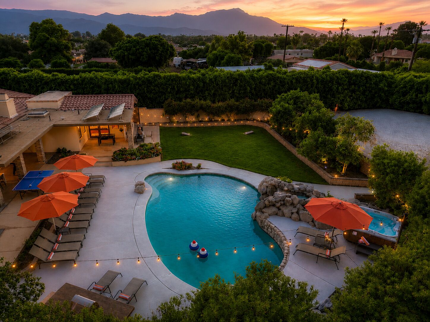 A swimming pool with lounge chairs and umbrellas, surrounded by a landscaped yard and a view of distant mountains.