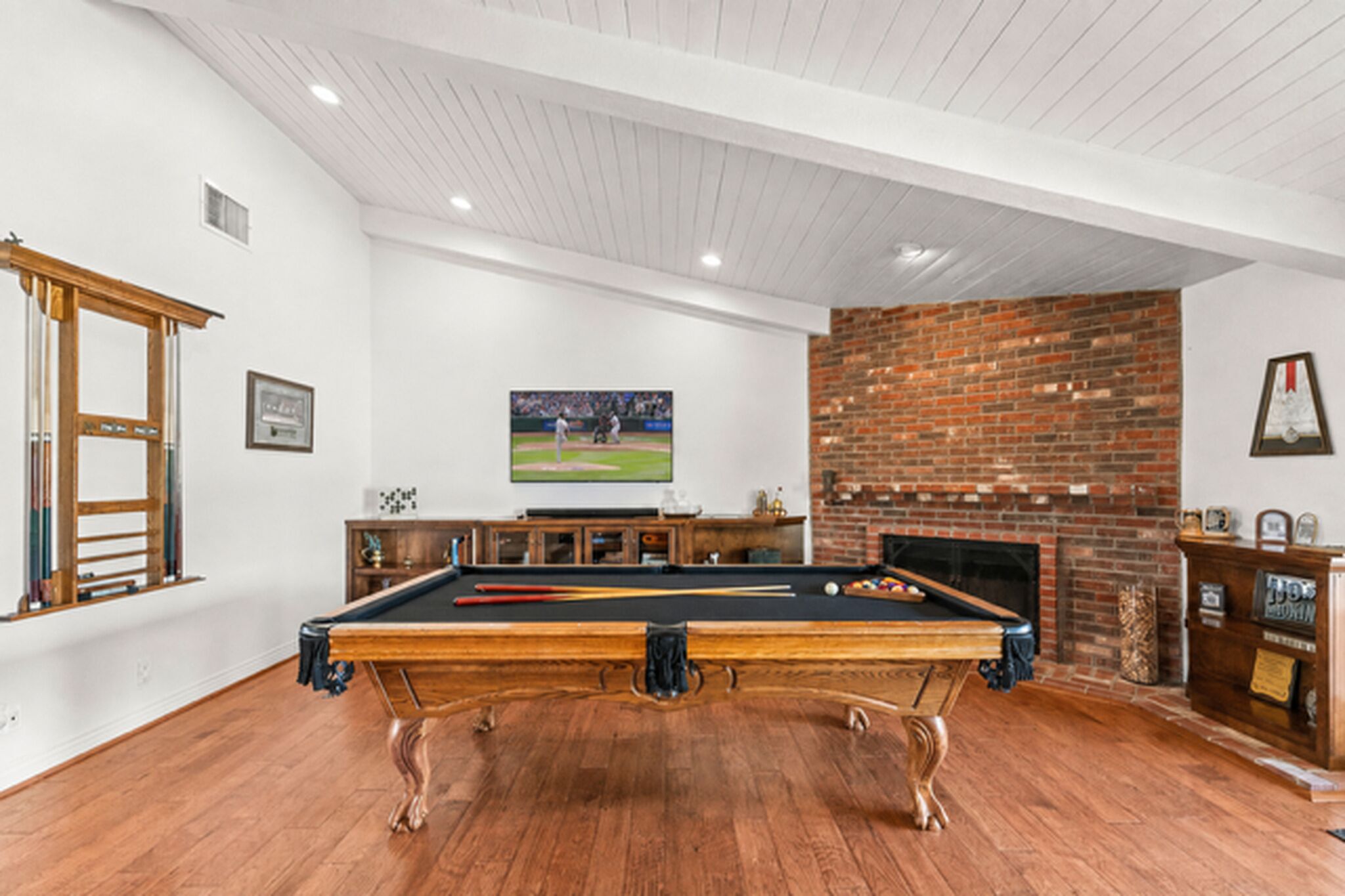 A pool table in a room with a brick fireplace and a framed picture on the wall.