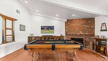 A pool table in a room with a brick fireplace and a framed picture on the wall.