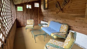 L'interno di una casetta in legno con un divano, due poltrone, un tavolino e due finestre con vetri decorati.