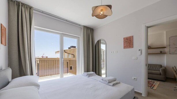 Hotellihuone, jossa on suuri sänky, parveke, jolta on näkymä rakennustyömaalle, sekä moderni valaisin.
