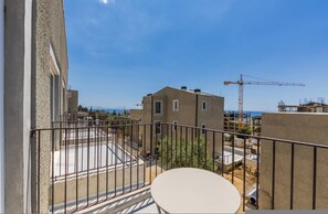 Ein Balkon mit Blick auf eine Baustelle und einen Kran, ein weißer Tisch und ein Gebäude mit flachem Dach.