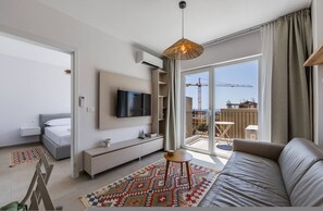 Ein modernes Apartment mit großem Fenster, einer Couch, einem Fernseher und einem gemusterten Teppich.