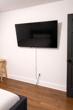 A room with a mounted television on the wall, a wooden stool, and a bed with a white mattress. - Cozy Home in East Atlanta (Atlanta)