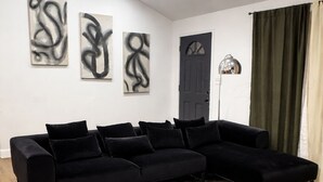 Una sala moderna con un sofá modular negro, una alfombra estampada en mármol, arte abstracto en la pared y una puerta oscura.
