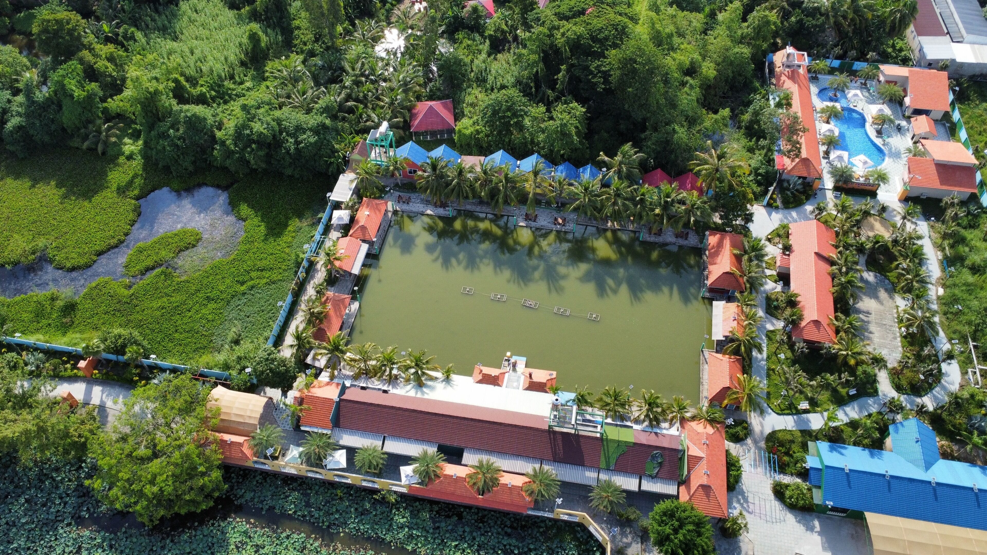 Vista aérea de un resort con un cuerpo de agua central, rodeado de abundante vegetación y varios edificios con tejados rojos.