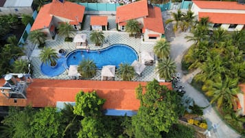 Vista aérea de un resort con piscina, palmeras y techo de tejas rojas.