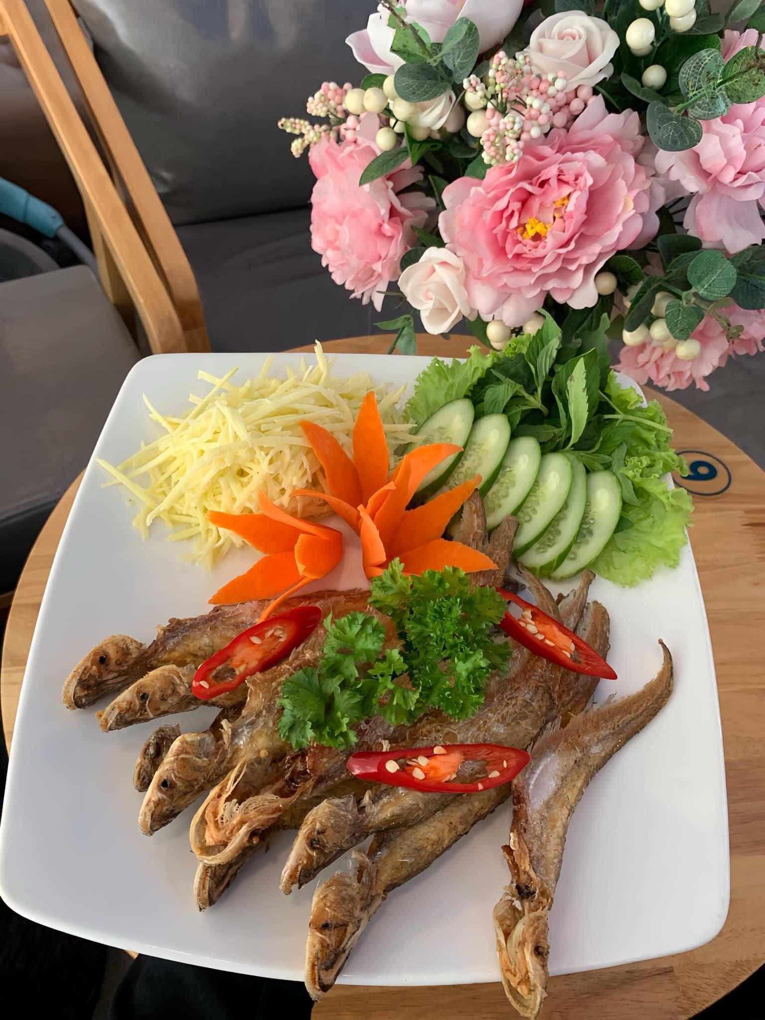 Une assiette contenant du poisson séché, des légumes et des fleurs.