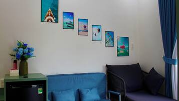 Una habitación con un sofá azul, una mesita con un florero y un refrigerador.