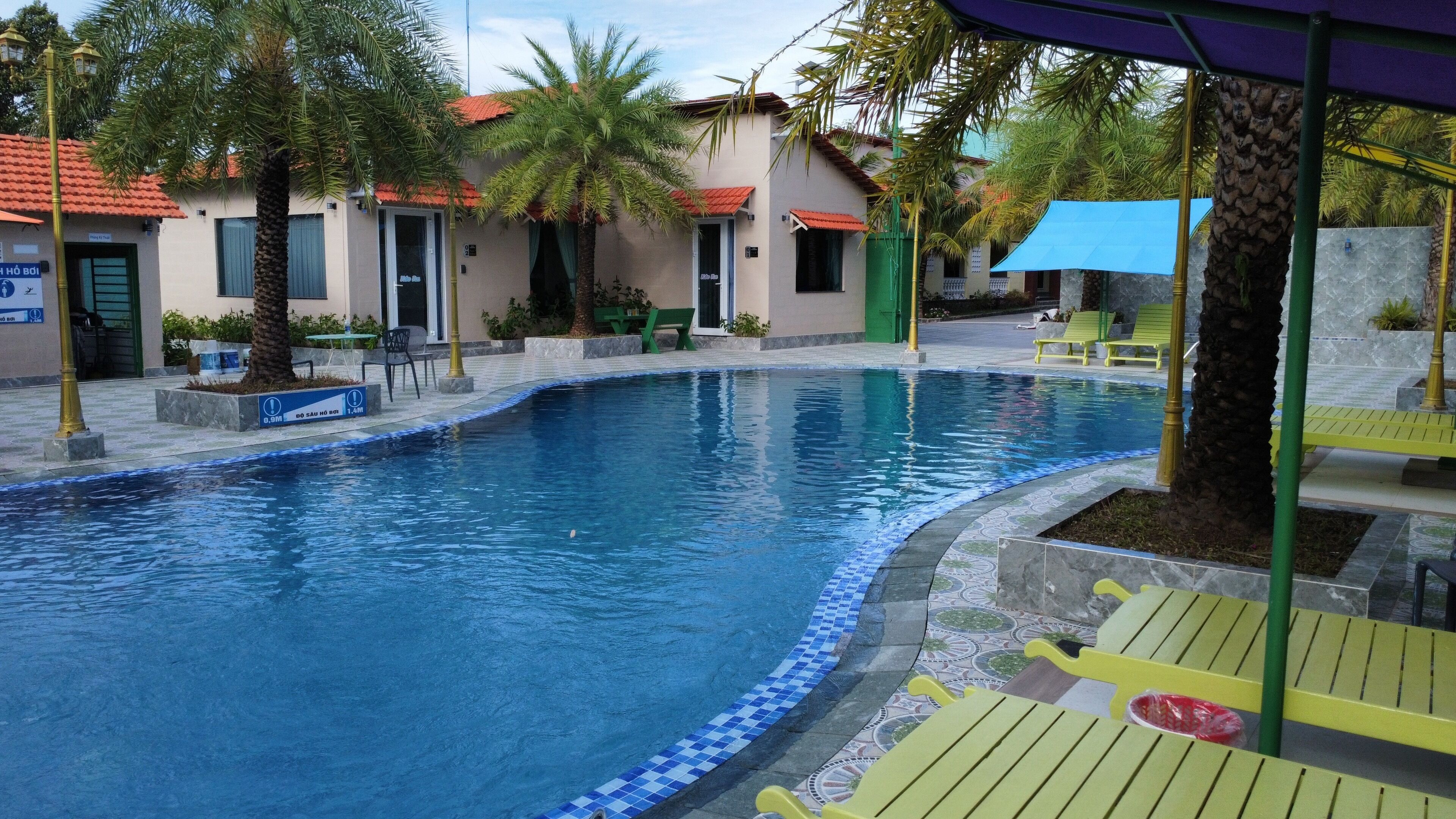 A swimming pool with a tiled edge, surrounded by palm trees and outdoor seating.