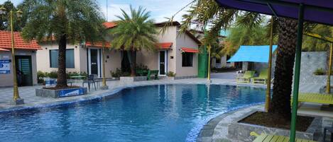 A swimming pool with a tiled edge, surrounded by palm trees and outdoor seating.