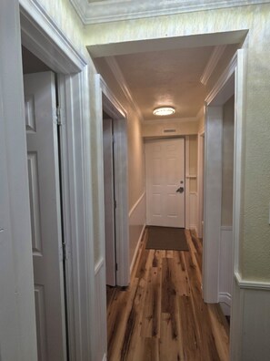 Un couloir avec un plancher en bois, des murs blancs et une porte blanche au fond.