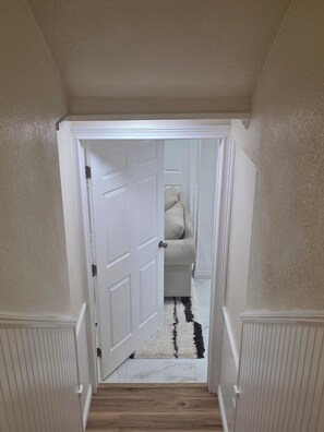 A hallway with a white door leading to a room with a beige sofa and a black and white rug. - EMARALD HAVEN (Fairbanks)