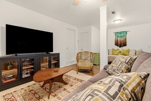A living room with a flat-screen TV, a wooden coffee table, a wicker chair, a patterned rug, and a sofa with decorative pillows. - Back40 Beehive: Bike-In Retreat-Trails, Lakes & Game Room (Bella Vista)