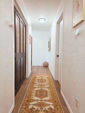 A hallway with a patterned rug, a door with a textured glass panel, and a wall-mounted light fixture. - Back40 Beehive: Bike-In Retreat-Trails, Lakes & Game Room (Bella Vista)