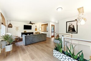 A spacious living room with a grey sofa, a ceiling fan, and a mounted TV. - Back40 Beehive: Bike-In Retreat-Trails, Lakes & Game Room (Bella Vista)