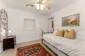 A bedroom with a bed, a ceiling fan, a nightstand with a lamp, a door, and a window. - Back40 Beehive: Bike-In Retreat-Trails, Lakes & Game Room (Bella Vista)