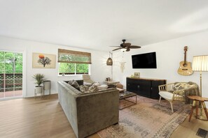 Ein Wohnzimmer mit einer Couch, einem Couchtisch, einem Fernseher, einer Gitarre und einem Deckenventilator.
