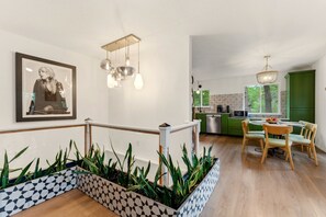 Una cocina moderna con armarios verdes, un comedor con sillas de madera y una escalera con barandilla.