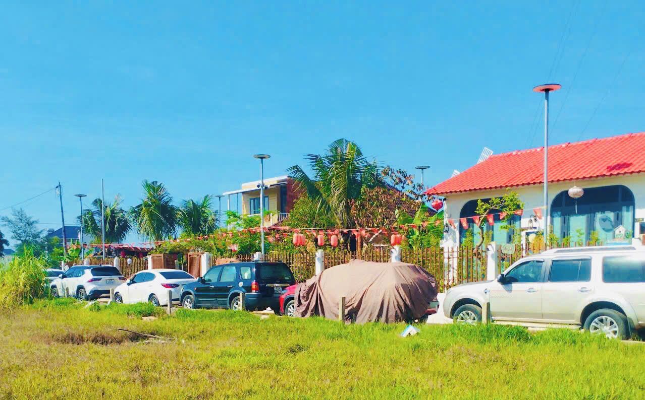 A parking lot with several cars, a covered vehicle, and buildings with red roofs in the background.