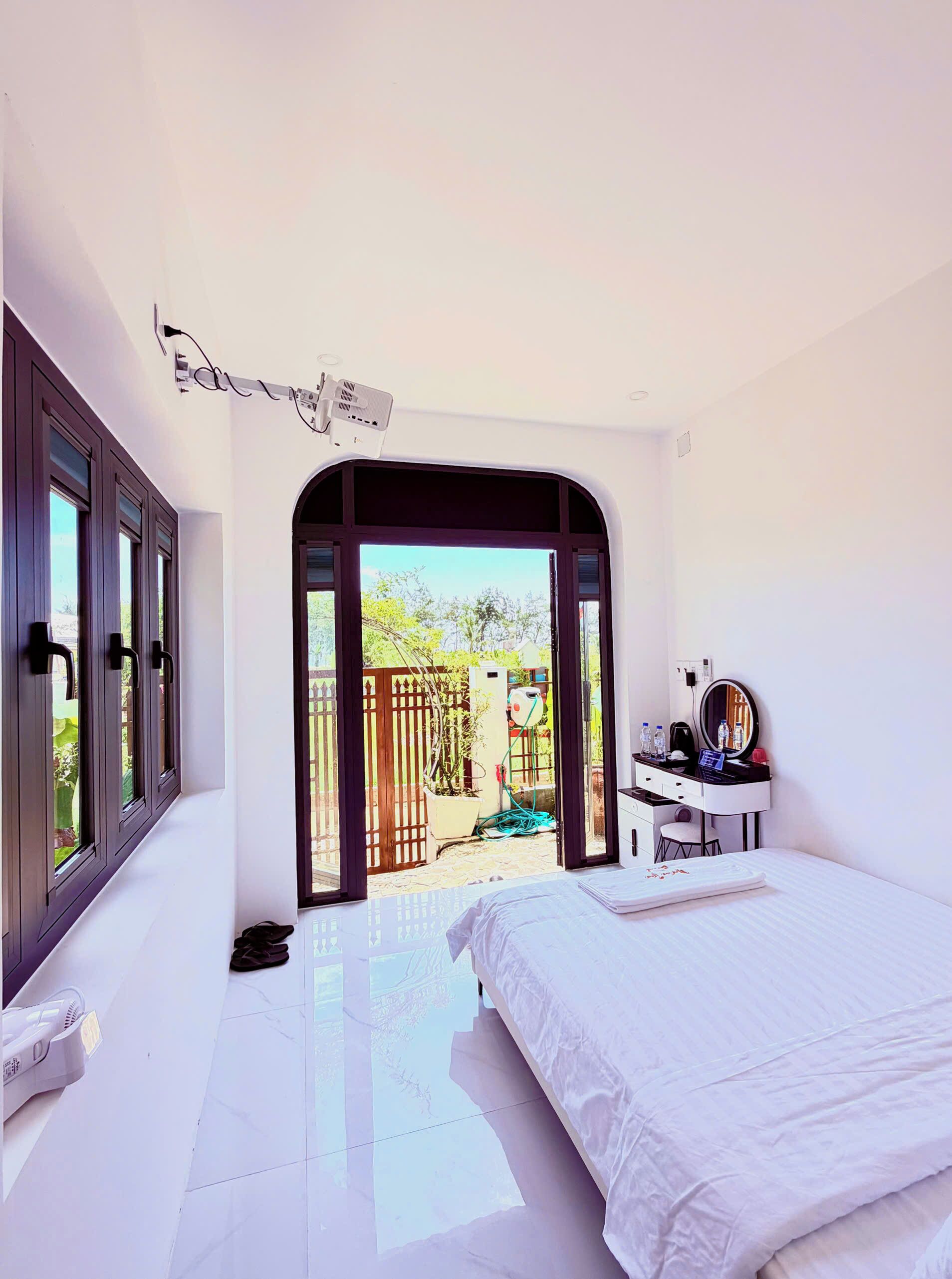 A bedroom with a bed, a desk with a mirror, and a view of the outdoors through a door.