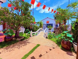 Un sendero que lleva a un edificio con fachada blanca y un emblema de estrella roja, rodeado de abundante follaje y plantas en macetas.