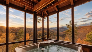 Ein Whirlpool in einer Holzhütte mit großen Fenstern mit Blick auf ein bewaldetes Tal.