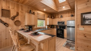 Ein Holzblockhaus-Interieur mit einer Küche, die eine Kochinsel, Holzschränke, einen Herd und einen Kühlschrank umfasst.