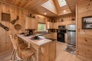 A wooden cabin interior with a kitchen featuring a central island, wooden cabinets, a stove, and a refrigerator. - Epic Views! 2 King Suites, Hot Tub, Privacy, location, pool table! Has it all! (Sevierville)