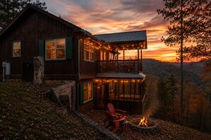 A wooden cabin with a balcony, a fire pit, and a scenic view of the forest. - Epic Views! 2 King Suites, Hot Tub, Privacy, location, pool table! Has it all! (Sevierville)