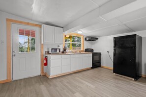 Eine Küche mit weißen Schränken, einem schwarzen Kühlschrank, einer Mikrowelle und einem Fenster mit Blick auf Bäume.