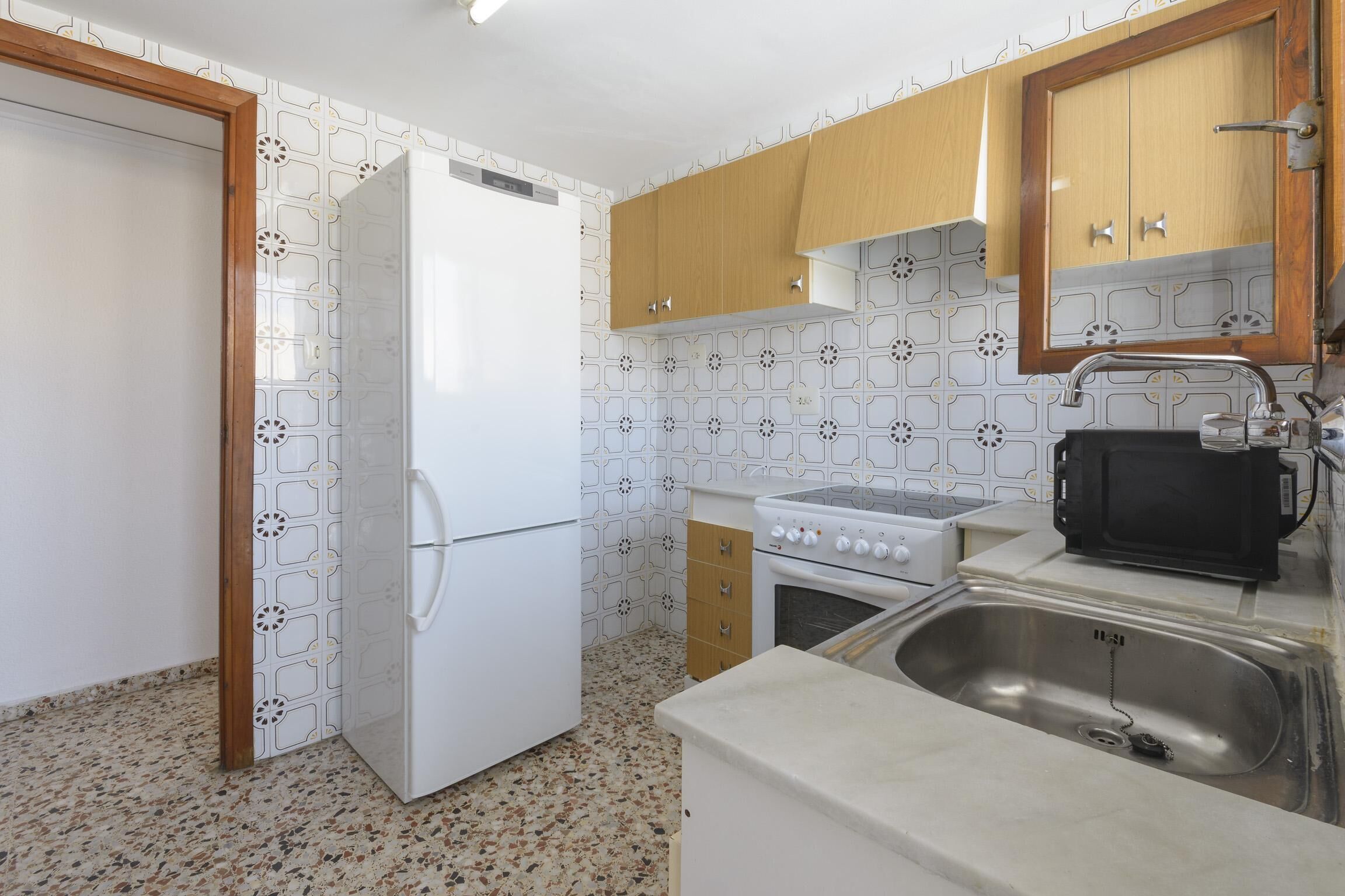 A kitchen with white appliances, wooden cabinets, a stainless steel sink, and patterned backsplash.