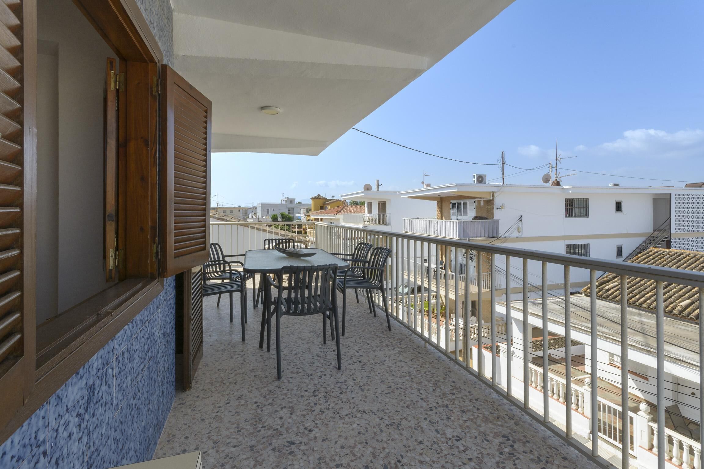Un balcón con mesa y sillas, vista a edificios vecinos y suelo de baldosas.