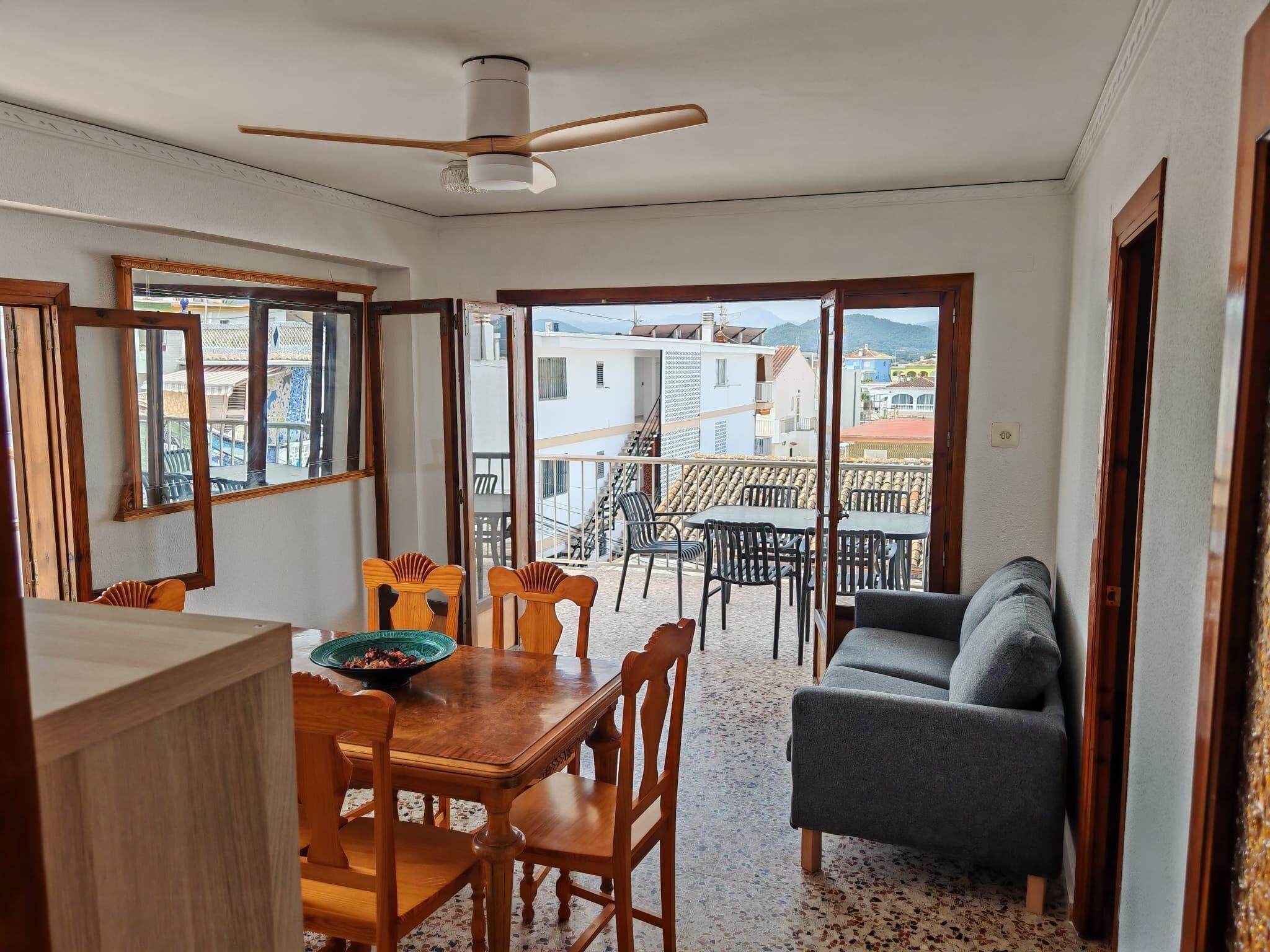 A dining area with a wooden table and chairs, a balcony with outdoor seating, and a ceiling fan.