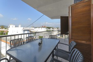 A balcony with a table and chairs, a view of buildings, and a closed shutter.