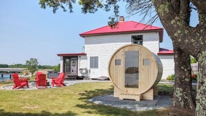 Una casa con techo rojo, una estructura de barril de madera y sillas Adirondack rojas.