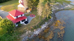 Una casa de dos pisos con techo rojo, un pequeño porche y un área con fogata.